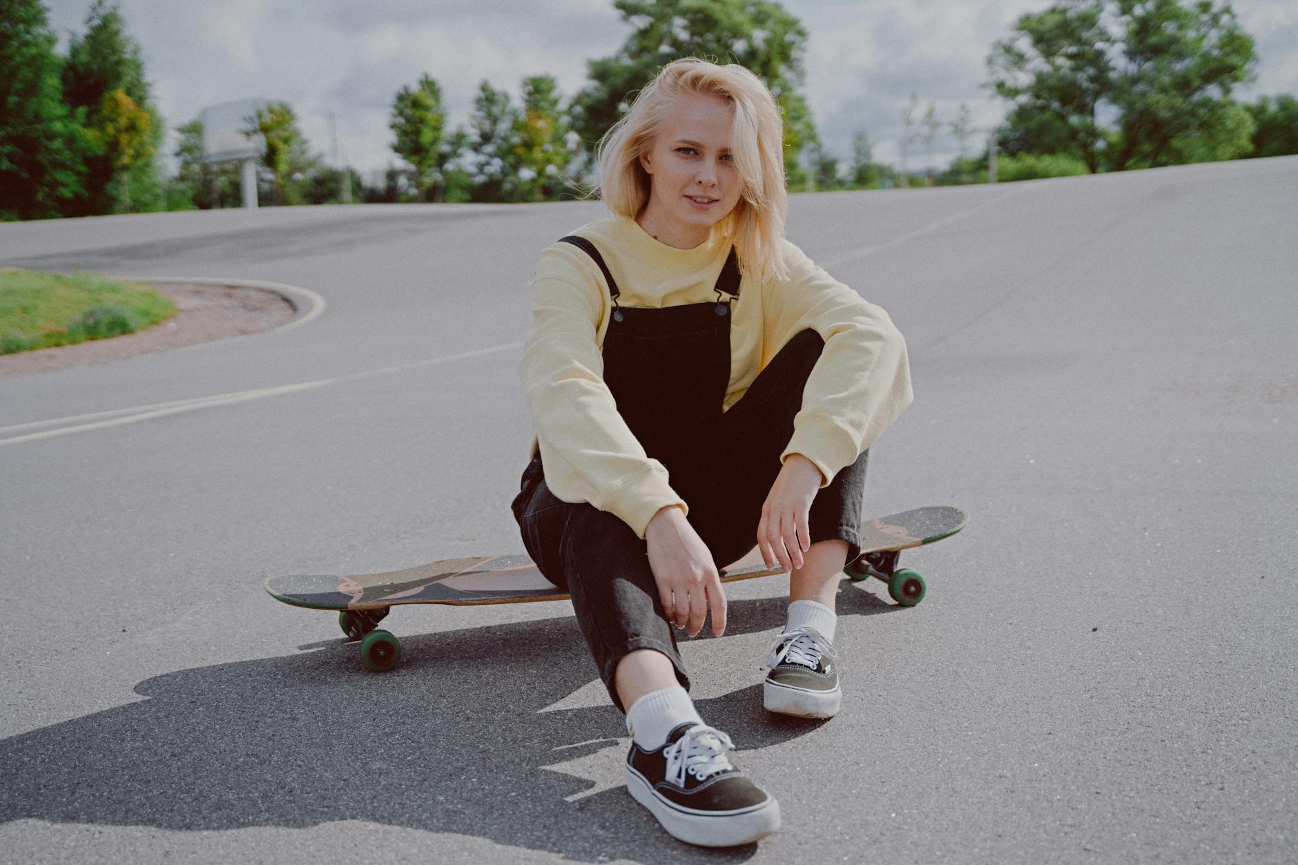 woman in a black jumper sitting on her longboard while looking at the camera